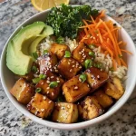 A colorful Buddha bowl filled with tofu, brown rice, edamame, shredded carrots, avocado, and kale, garnished with sesame seeds and cilantro.