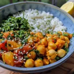 Close-up view of a vibrant bowl of turmeric and chickpeas garnished with sesame seeds and almond slices.