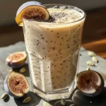 Close-up side view of a creamy fig smoothie in a glass, adorned with fresh figs.