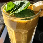 Close-up view of a vibrant ginger smoothie in a glass, showcasing its thick texture and color.