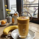 Close-up view of a creamy pumpkin smoothie with apple and orange in a glass.