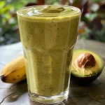 Close-up side view of a creamy banana and avocado smoothie in a glass.