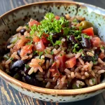 Close-up view of a bowl filled with dark black rice, topped with colorful cherry tomatoes and avocado.